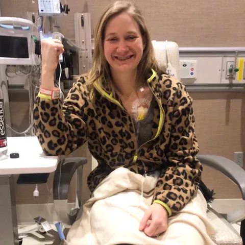 Blonde woman in hospital bed smiles while receiving chemotherapy